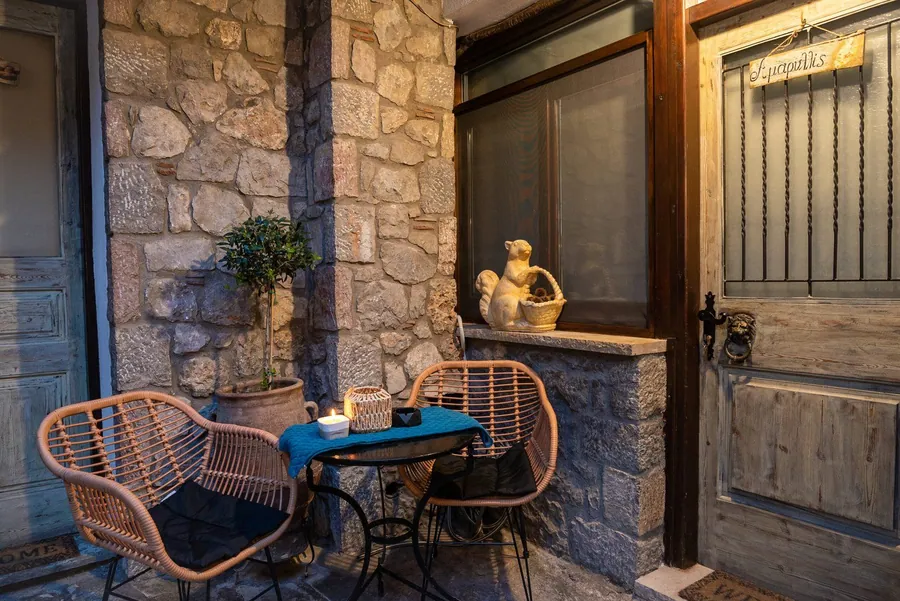 Πέτρινη γωνιά της αυλής με ψάθινες καρέκλες, τραπεζάκι και ξύλινη πόρτα